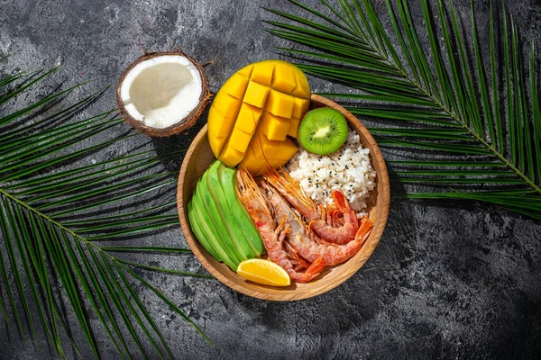 tropical bowl with avocado, prawns, rice, mango, kiwi and coconut, tropical food on the sea beach, Organic and healthy food, place for text, top view,