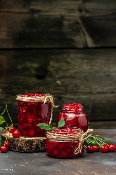 Fresh red cherries fruit on wooden background. Jar of cherry jam and sour cherries. Berries cherry with syrup. Canned fruit. place for text, top view.