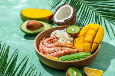 Poke bowl with avocado, shrimp, rice, mango, kiwi and coconut on a blue background, healthy and balanced food. banner, menu recipe place for text, top view