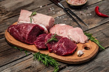 raw pork meat and beef with rosemary and spices on a wooden board. Restaurant menu, dieting, cookbook recipe. place for text.