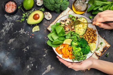 Elinde vejetaryen kahvaltısı olan bir kız. Avokado, mantar, brokoli, ıspanak, nohut, balkabağı. en üstteki görünüm.