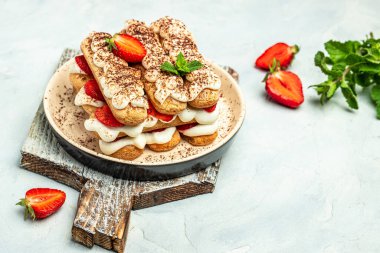 Italian dessert tiramisu cake with fresh strawberry, biscuit and whipped cream and mint on a light background, Vegan lactose free dessert.