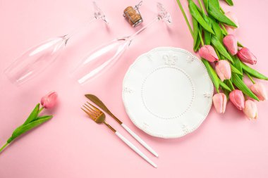 Annelerin gündüz masası pembe arka plana beyaz tabak ve çiçekler koyuyor..