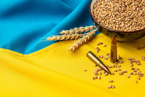 Пули и зерно на фоне желто-синего украинского государственного флага. Концепция продовольственного кризиса и глобального дефицита продовольствия. место для текста, вид сверху