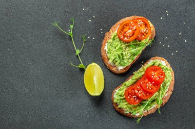 Avokado sandviçi koyu arkaplanda domatesle yapılan koyu çavdar ekmeği. en üstteki görünüm,