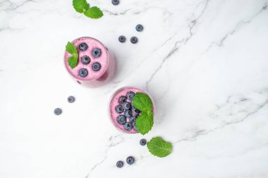 Böğürtlenli yoğurt, bardakta taze yaban mersini, nane yaprağı ve beyaz arka planda çiğ bira. Restoran menüsü, diyet, yemek kitabı tarifi üst görünümü.