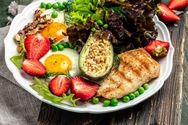 Sağlıklı besleyici paleo keto kahvaltı diyeti kızarmış yumurta, avokado, ızgara tavuk fileto, fındık, çilek ve taze salata. Keto kahvaltısı ya da öğle yemeği. en üstteki görünüm,