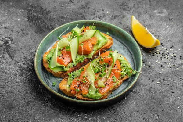 stock image two toasts with salted salmon, guacamole avocado and fresh greens on plate. superfood concept. Healthy, clean eating. Vegan or gluten free diet. top view.