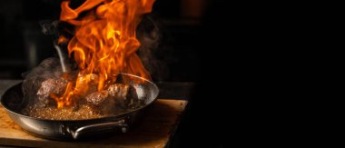 Beef steaks on the grill pan with flames on a dark background. Long banner format.