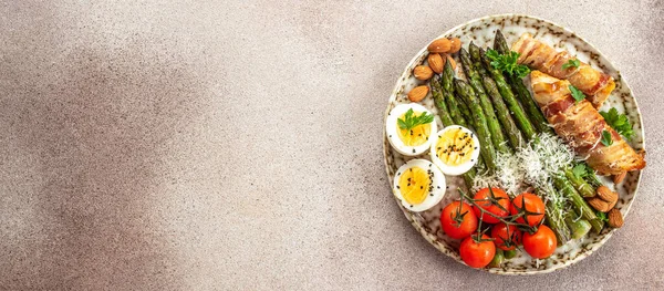 stock image Baked chicken breast wrapped in bacon with asparagus, eggs and tomatoes. Ketogenic diet. Low carb high fat breakfast. Healthy food concept. Long banner format. top view,