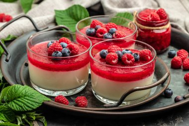 Küçük kavanozlarda koyu arka planda böğürtlen soslu lezzetli İtalyan tatlı panna cotta. metin için yer.