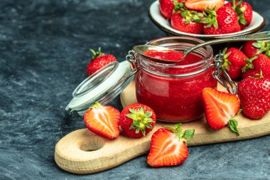 Cam kavanozda çilek reçeli, ev yapımı çilekli marmelat ve koyu arka planda meyveler, üst manzara. metin için yer,