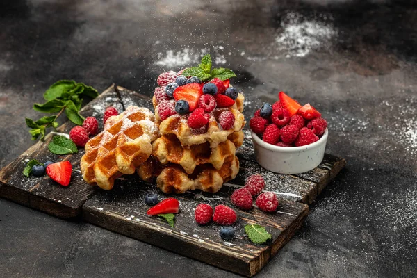 Belgian waffles with raspberries, strawberries and blueberries, sugar powder over black background.