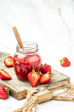 Cam kavanozda çilek reçeli ve beyaz masada bir kaşık. dikey görüntü. en üstteki görünüm,
