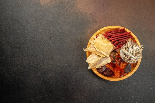 snacks for beer, Dried fish mix on wood plate. dried fish chorizo sausage meat carpaccio on a dark background. place for text, top view.