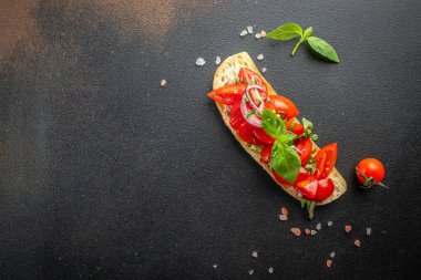 Domatesli İtalyan aperatifleri ya da koyu arkaplanda fesleğenle süslenmiş kızarmış baget dilimleri üzerinde bruschetta. afiş, menü, metin için tarif yeri, üst görünüm.