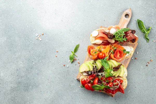 stock image a set of bruschetta with prosciutto, salmon, tomatoes and avocado on a wooden board, banner, menu, recipe place for text, top view,