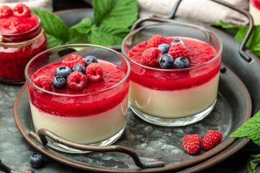 Ahudududulu panna cotta, üzerinde ahududu reçeli ve koyu bir arka plan. Küçük kavanozlarda krema soslu böğürtlen tatlısı. metin için yer.