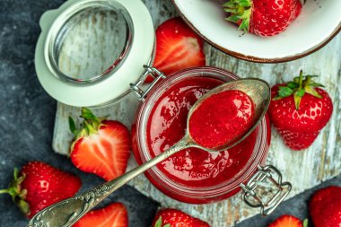 Cam kavanozda çilek reçeli, ev yapımı çilekli marmelat ve koyu arka planda meyveler, üst manzara. metin için yer,