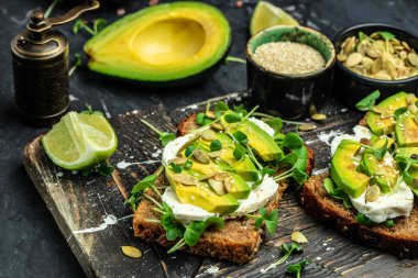 Vejetaryen sandviçler. Avokado tostları koyu arkaplanda çavdar ekmeği, lezzetli kahvaltı ya da atıştırmalık, temiz yemek, diyet, vegan gıda konsepti. en üstteki görünüm.