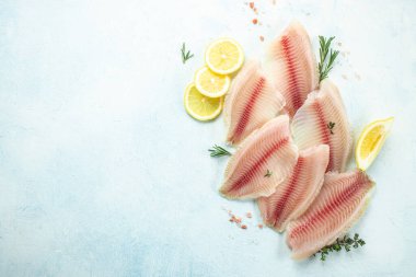 Telapia 'nın çiğ filetosu ya da arka planda limon ve baharatlı pangasius. afiş, menü, metin için tarif yeri, üst görünüm.