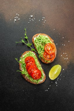 Avokado sandviçi koyu arkaplanda domatesle yapılan koyu çavdar ekmeği. dikey görüntü. Üst Manzara. metin için yer,