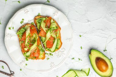 Krem peynirli sandviç, somon, avokado, salatalık, domates ve açık arkaplanda yeşillikler. Keto kahvaltısı ya da brunch. afiş, menü, metin için tarif yeri, üst görünüm.