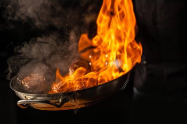 Izgarada biftekler, alevler ve karanlık bir arka planda buharlar.,