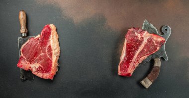 Siyah taşlı arka planda et bifteği ve bıçak arasında bir kemik. Çiğ et. Uzun afiş biçimi. Üst görünüm, metin için yer, üst görünüm,