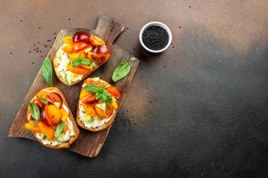 Tost, aperatif, bruschetta, krem peynirli sandviç, şeftali, domates ve yeşil fesleğen yaprağı, sağlıklı ve dengeli yeme kavramı. metin için yer, üst görünüm,