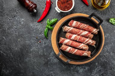 Koyu bir arka planda pastırmaya sarılmış domuz eti. afiş, menü, metin için tarif yeri, üst görünüm.