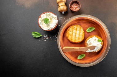 Krem peynirli kızarmış ekmek ve koyu arkaplanda taze fesleğen yaprağı. afiş, menü, metin için tarif yeri, üst görünüm.