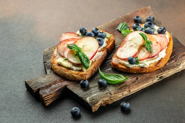 Krem peynirli tost, bal, şeftali ve böğürtlen ahşap bir tahtada, yazı için yer, üst görünüm,