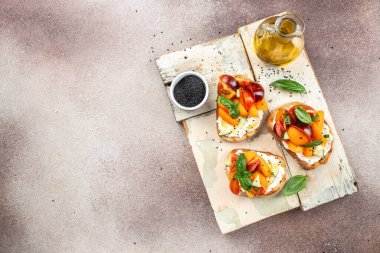 Tost, aperatif, bruschetta, krem peynirli sandviç, şeftali, domates ve yeşil fesleğen yaprağı, sağlıklı ve dengeli yeme kavramı. metin için yer, üst görünüm,