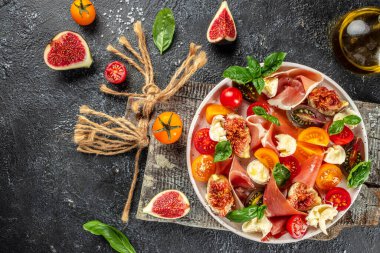 Mozarella, incir, prosciutto, taze fesleğen yaprağı ve domatesli ev yapımı salata. afiş, menü, metin için tarif yeri, üst görünüm.
