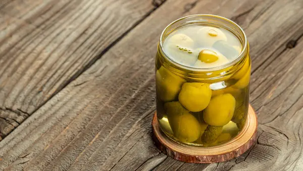 Glass Jar of Pickled Vegetables Olives with cucumbers on a rustic wooden table. Long banner format. top view.