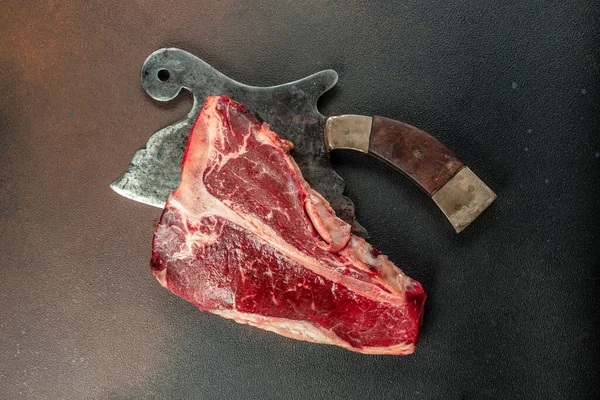 Ahşap bir tahtanın üzerinde büyük çiğ biftek. Biftek ve arka planda et satırı. en üstteki görünüm.