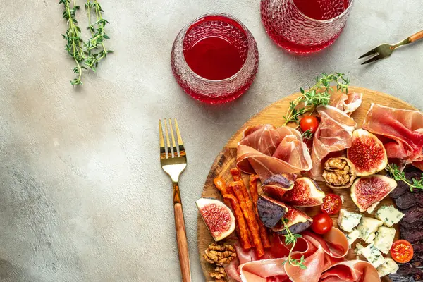 Rose wine with prosciutto, ham snack slices with figs and cheese on a light background top view. place for text,