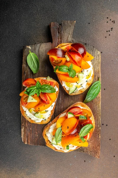Gourmet sandwiches bread toast, bruschetta with cream cheese, peaches, tomatoes and green basil leaves on a wooden board. vertical image. top view. place for text.