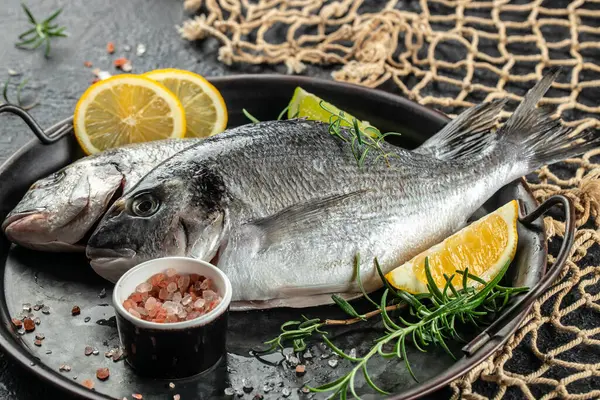 Fresh uncooked dorado or sea bream fish with lemon on a dark background. Restaurant menu, dieting, cookbook recipe top view.