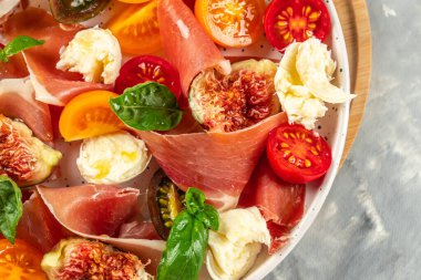 Mozarella, incir, prosciutto, taze fesleğen yaprağı ve domatesli diyet salatası, yemek tarifi geçmişi. Kapat.,