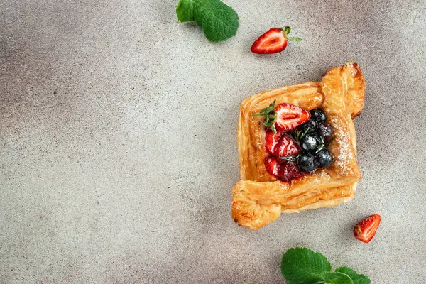 square fruit filled French puff pastry dessert with berries on a light background. banner, menu, recipe copy space, top view.