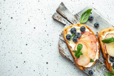 Krem peynirli, ballı, şeftalili ve yaban mersinli lezzetli tost. Sağlıklı ve dengeli beslenme kavramını arka planda açık arka planda tut. Boşluğu kopyala.