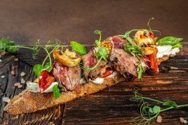 Biftekli sandviç, dilimlenmiş biftek, mantar, kurutulmuş domates, salatalık turşusu ve koyu arkaplanda yeşillikler. Üst Manzara. metin için yer,