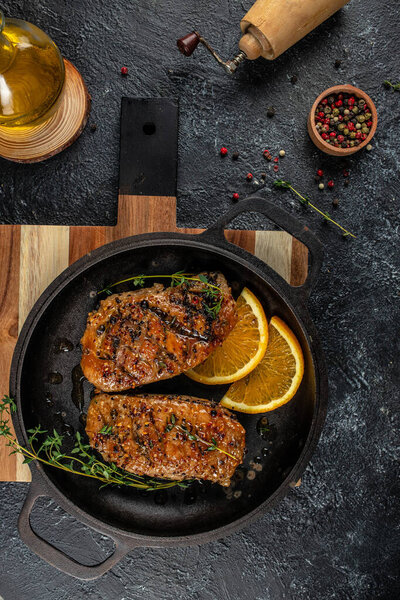 roasted duck meat steak with oranges and thyme in a pan. on a dark background. vertical image. top view. copy space for text.