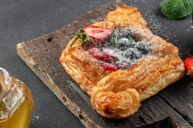 Koyu arkaplanda taze böğürtlenli puf böreğinden yapılmış küçük bir açık turta, yemek tarifi geçmişi. Kapat.,