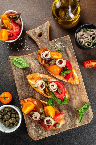 sandwich with marinated anchovies and fresh tomato, olive oil on a wooden board. vertical image. top view. copy space for text.