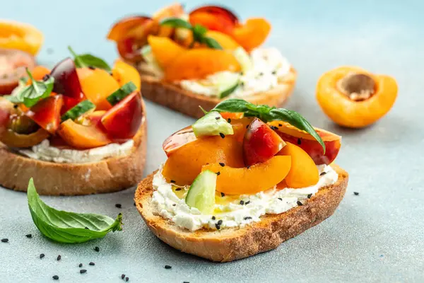 Open sandwiches with cream cheese, peaches, tomatoes and green basil leaves on a light background, top view.