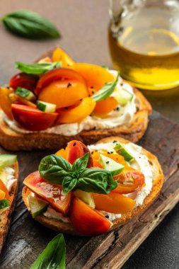 Tost, aperatif, bruschetta, krem peynirli sandviç, şeftali, domates ve yeşil fesleğen yaprağı, sağlıklı ve dengeli yeme kavramı. metin için yer, üst görünüm,