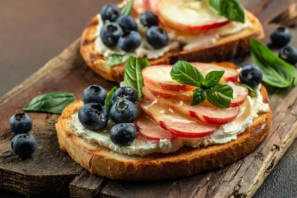 toast with cream cheese, honey, peaches and blueberries on a wooden board, place for text, top view,